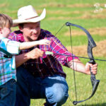 Man teaching a kid how to shoot a bow and arrow